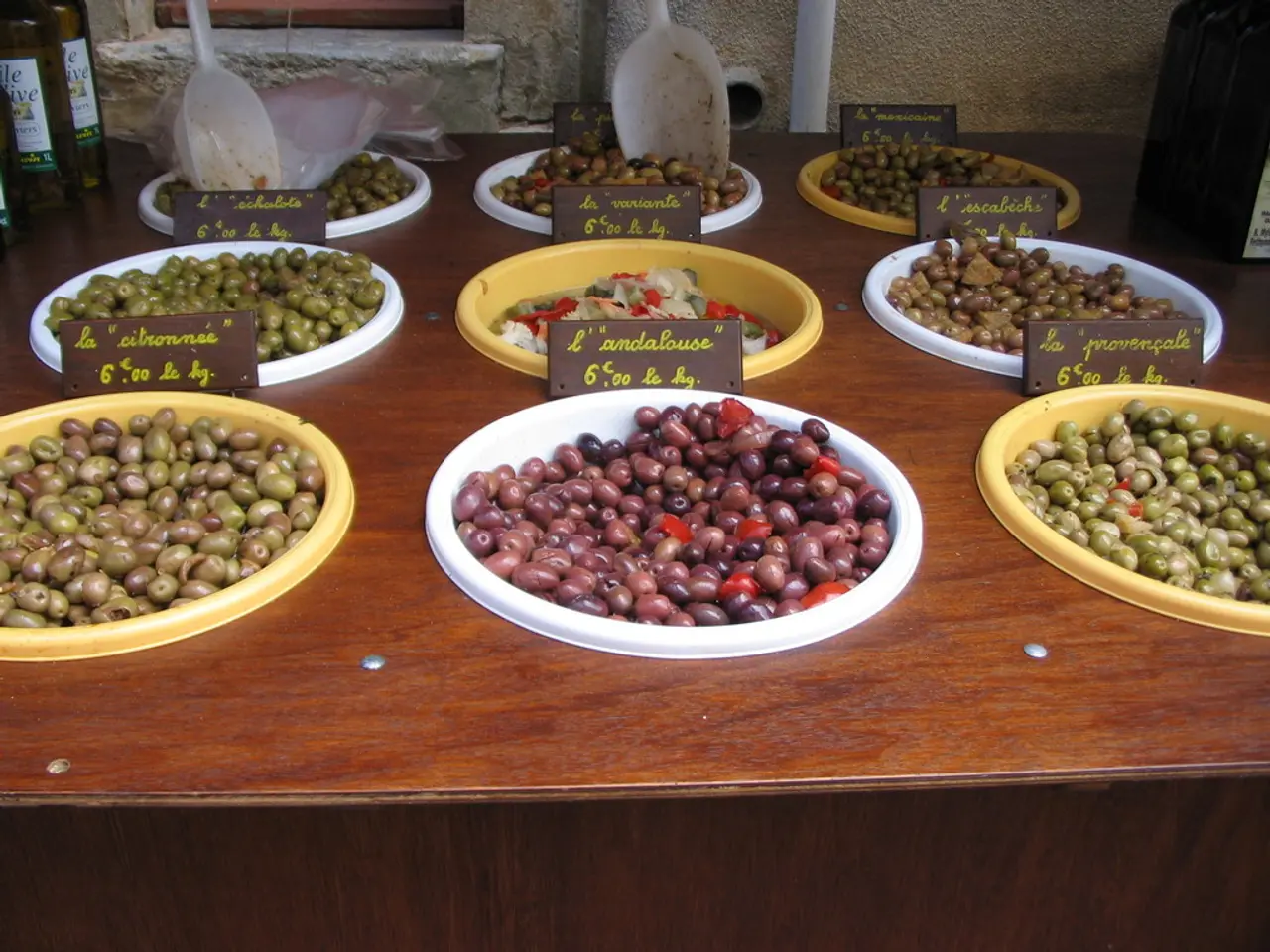 In this image there is a wooden table. On the table there are olives and fruits in the bowls....