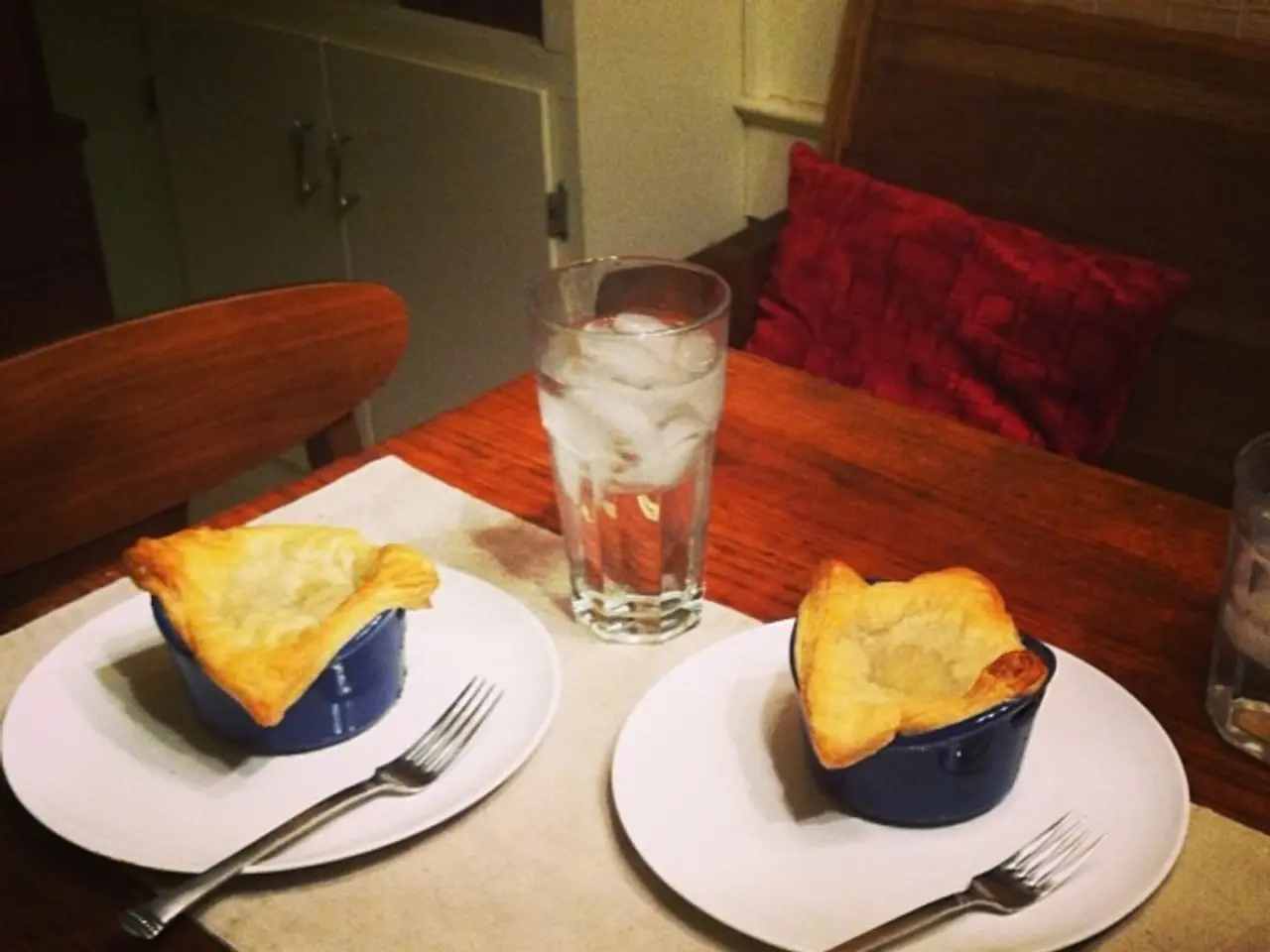 In the center of the image there is a dining table. There are plates, forks, cups, glasses and some...