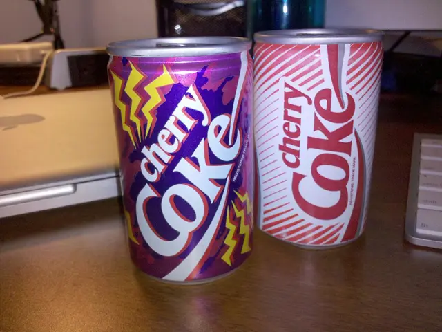 In the image there are two coke tins, keyboard, laptop kept on a table.