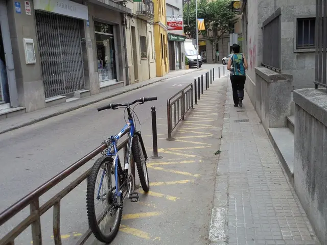 As we can see in the image there are buildings, bicycle, car, van, flag, banner, a person walking...